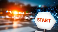 Glowing hexagonal start sign with digital network overlay against blurred urban traffic background at dusk, representing business beginnings and technology innovation.