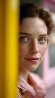 Young Caucasian woman with freckles and blue eyes looking thoughtfully through yellow window frame in soft natural light for lifestyle photography.