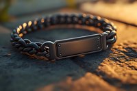 Black metal chain bracelet with rectangular plate on textured surface in warm sunset lighting, macro jewelry photography showing fine details and craftsmanship.