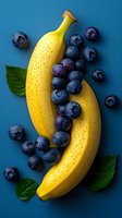 Fresh ripe bananas and blueberries with green leaves arranged on blue background. Healthy eating concept for food industry and marketing materials.