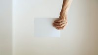 Male hand holding blank white card or paper against neutral background, suitable for mockups, advertising, and promotional designs.