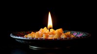Lit oil lamp with glowing flame and golden resin chips in decorative metal bowl against dark background, suitable for spiritual and wellness design projects.