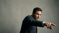 Confident middle-aged Caucasian businessman in dark suit pointing forward with determined expression against neutral background for corporate presentations.
