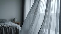Sheer gray curtains flowing in modern bedroom with unmade bed and minimalist decor, suitable for interior design and home styling projects.