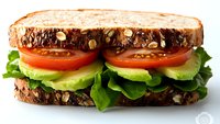 Fresh vegetable sandwich with whole grain bread, sliced tomatoes, avocado, and crisp lettuce on white background, appetizing healthy lunch option.