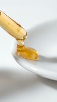 Golden honey dripping from wooden dipper onto white ceramic bowl, showcasing natural sweetener for culinary, wellness, and food styling applications.