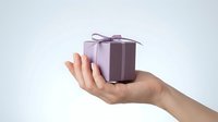 Female hand holding small purple gift box with ribbon bow on white background for holidays and celebrations.