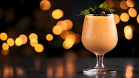 Creamy orange cocktail garnished with fresh mint and blackberries in elegant glass against warm bokeh lights background for bar menu design.