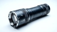 Black tactical flashlight with textured grip and bright LED light isolated on white background for emergency preparedness and outdoor activities.