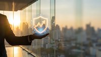 Businessman holding glowing shield icon with upward arrow above city skyline at sunset, representing data security, growth, and financial protection for business concepts.