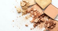 Crushed makeup powder cosmetics in warm nude and bronze tones scattered on white background for beauty and fashion applications.