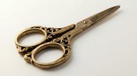 Vintage brass embroidery scissors with ornate handles and sharp blades, isolated on white background for crafting, sewing, and needlework design projects.