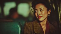 Young Asian businesswoman in brown blazer smiling confidently in modern office environment with warm lighting for corporate and professional concepts.