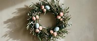 Festive olive branch wreath with pink and dark ornaments casting shadows on neutral wall for holiday home decor and seasonal celebrations.