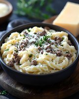 Creamy pasta with ground beef, parmesan cheese and fresh herbs served in dark ceramic bowl on wooden board. Traditional Italian cuisine comfort food.