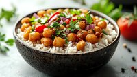 Spicy chickpeas with rice in black bowl garnished with fresh herbs, red onion, and tomatoes. Mediterranean style vegetarian meal with aromatic spices and herbs.