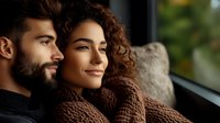 Young mixed race woman with curly hair and Hispanic man with beard embrace near window, expressing tender romantic relationship and connection.