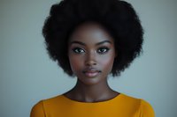 Young African American woman with natural afro hairstyle wearing yellow top against neutral background, looking directly at camera with confident expression.
