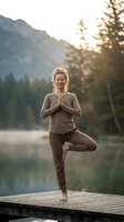 Peaceful young Caucasian woman practicing tree pose yoga on wooden dock at mountain lake during golden hour sunrise meditation session for wellness and mindfulness.
