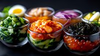 Korean side dishes in glass bowls featuring kimchi, seaweed, pickled vegetables, boiled egg and fresh cucumber arranged on dark background for authentic Asian cuisine.