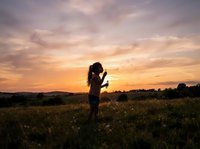 Silhouetted female photographer with camera capturing sunset over wildflower meadow during golden hour, suitable for photography, travel, and nature editorial content.