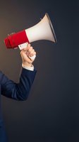 Businessman in navy suit holding red and white megaphone against dark background, representing announcement, communication, marketing message, and business promotion strategy.