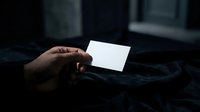 Hand holding blank white business card in dark moody lighting for branding mockup and corporate identity design projects.