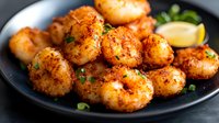 Spicy seasoned shrimp served on black plate with fresh herbs and lemon garnish, close up view of crispy fried seafood appetizer in warm lighting.
