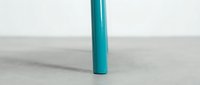 Turquoise blue cylindrical tube or pipe standing vertically on concrete surface against white wall background for modern industrial design projects.