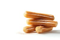 Fresh churros dusted with sugar stacked on white background, golden-brown Spanish pastry dessert isolated for food photography and menu design.