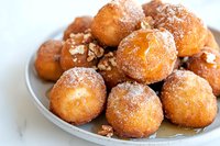 Fresh homemade sugar-coated donut holes sprinkled with crushed walnuts served on gray ceramic plate against white marble background. Perfect for food blogs.