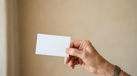 Mature hand holding blank white card against neutral beige background for business, marketing, and promotional mockup designs.