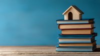 Small wooden house model sitting atop stack of books against blue background, symbolizing home education, knowledge building, and property investment concepts.