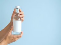 Person holding clear water bottle with white label against blue background, suitable for beverage, hydration, wellness and product packaging mockup designs.
