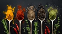 Colorful spices and herbs arranged in wooden spoons on dark background. Turmeric, paprika, cumin, peppercorns and green powder with fresh herbs for cooking.
