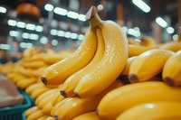 Fresh ripe yellow bananas on display at grocery store produce section with soft bokeh background lighting, close-up view showing natural texture and shine.