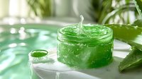 Fresh green aloe vera gel with water splash in transparent jar on marble surface with natural plant leaves in soft daylight, skincare concept.
