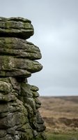 Stacked moss-covered rock formation with distinctive layered appearance against moorland landscape, suitable for nature and geology projects.