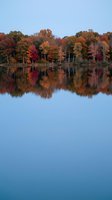 Tranquil lake reflecting vibrant autumn foliage in orange, red and yellow hues with perfect mirror-like water surface creating stunning fall landscape symmetry.