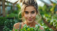 Young woman with messy bun hairstyle smiling in greenhouse surrounded by green plants, perfect for lifestyle, beauty, and natural cosmetics advertising.