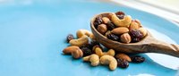 Mixed nuts and dried fruits in wooden spoon on blue background. Healthy snacking, organic food ingredients for cooking and baking recipes.