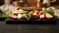 Fresh spring salad with grilled asparagus, radishes and hard-boiled eggs on dark slate board. Healthy vegetarian meal with seasonal vegetables and greens.