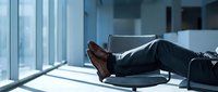 Businessman relaxing with feet up on desk in modern office with large windows and natural light creating professional workspace atmosphere.