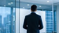 Professional businessman in dark suit standing at office window overlooking city skyline, corporate leadership and business success concept for presentations.