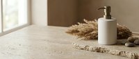 White ceramic soap dispenser bottle on natural jute mat with dried pampas grass and stones in minimalist bathroom setting with warm sunlight.