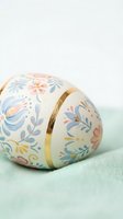 Hand-painted Easter egg with delicate floral pattern and gold ribbon on soft mint green fabric background for spring holiday celebrations.