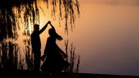 Romantic couple dancing silhouette under weeping willow tree at golden sunset creating heart shape with arms for wedding anniversary celebration.