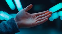 Open palm of Caucasian person wearing grey sweater against blurred cyan neon lights background creating moody atmospheric composition for technology and future concepts.