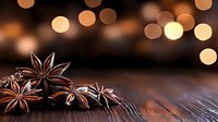 Star anise pods on rustic wooden surface with warm glowing bokeh lights in background creating festive holiday atmosphere for seasonal cooking and decoration.