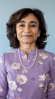 Middle-aged Asian woman wearing lavender floral dress and pearl necklace smiling warmly at camera against light background, expressing confidence and joy.